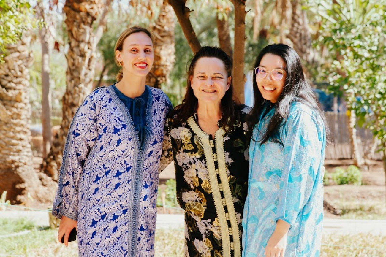 Three women of Amal smiling together among the palm trees in the garden