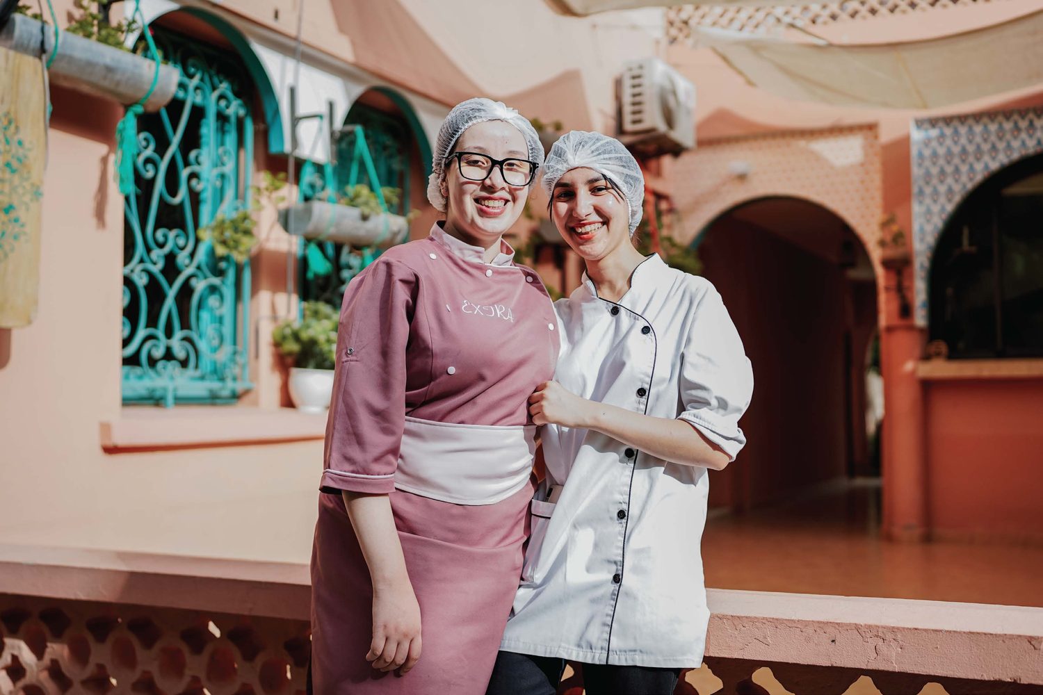 Two Amal chefs arm in arm in the riad courtyard