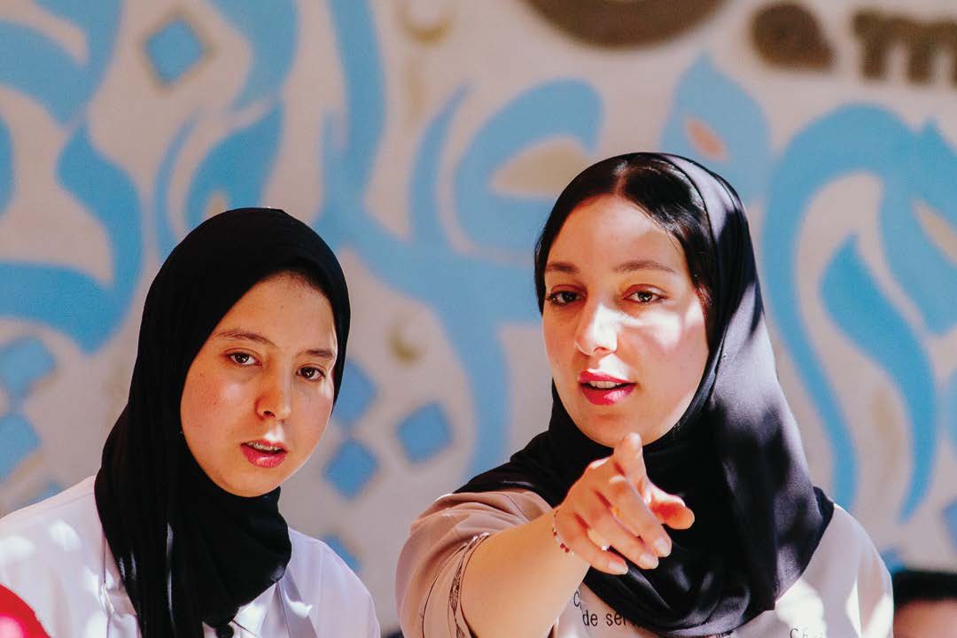 Two smiling women of the Amal community in front of a colourful mural